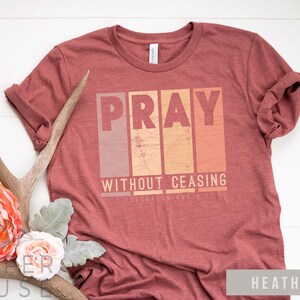 Op de afbeelding: Een heather clay t-shirt met de tekst "Pray Without Ceasing" in een vintage grafische stijl. De tekst is in een bloklettertype met een vervaagde, verweerde look.