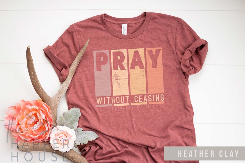 Op de afbeelding: Een heather clay t-shirt met de tekst "Pray Without Ceasing" in een vintage grafische stijl. De tekst is in een bloklettertype met een vervaagde, verweerde look.