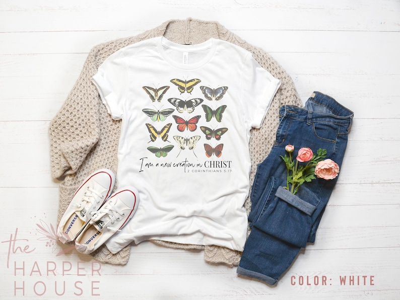 Puede incluir: Camiseta blanca con un gr&aacute;fico de mariposas de colores y el texto "Soy una nueva creaci&oacute;n en CRISTO 2 Corintios 5:17".