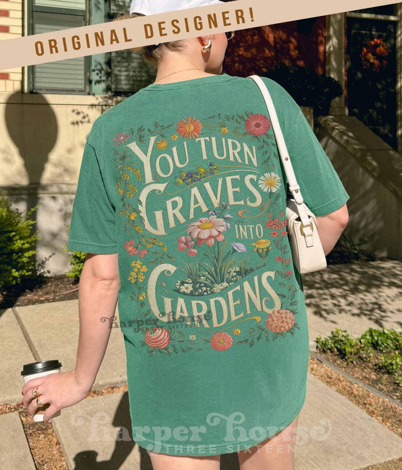 May include: Green t-shirt with the text "You Turn Graves Into Gardens" in a floral design. The shirt has a vintage aesthetic and is made of a soft material. The words "Original Designer" are printed at the top.
