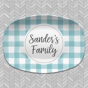 May include: A white oval serving platter with a blue and white gingham pattern. The center of the platter has a circle with the text "Sander's Family" in black.