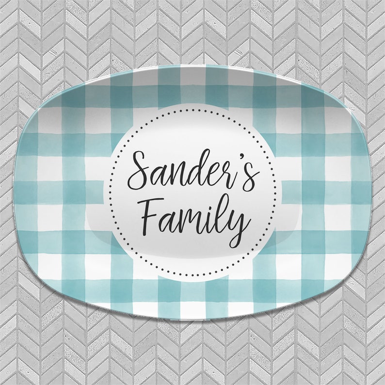May include: A white oval serving platter with a blue and white gingham pattern. The center of the platter has a circle with the text "Sander's Family" in black.