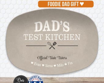 May include: An oval-shaped light brown serving platter featuring the white text DAD'S TEST KITCHEN, a whisk and spatula graphic, and the text Official Taste Testers followed by the names Evan, Siena, Milo, and Fin separated by heart and paw icons.