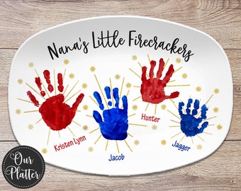 May include: White oval serving platter with the text "Nana's Little Firecrackers" in black lettering.  Four handprints are displayed in red and blue paint with gold stars and the names "Kristen Lynn", "Jacob", "Hunter", and "Jagger" written below each handprint.