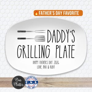 May include: An oval white ceramic serving platter featuring a black graphic of a grilling fork and spatula. The text reads DADDY'S GRILLING PLATE, HAPPY FATHER'S DAY 2026, and LOVE, MAX & RUBY. An orange banner at the top displays FATHER'S DAY FAVORITE.