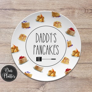 May include: White ceramic plate with a black and white design that says "Daddy's Pancakes" with a spatula graphic. The plate is decorated with watercolor illustrations of pancakes with blueberries and fruit.