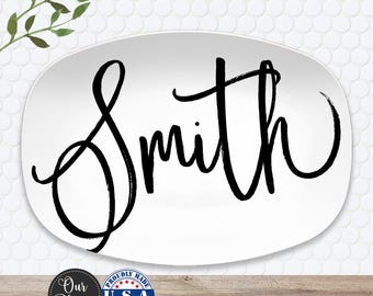 May include: White oval platter with the name "Smith" in large, black, cursive lettering. The platter has a simple, elegant design, suitable for serving food. The platter is proudly made in the U.S.A.