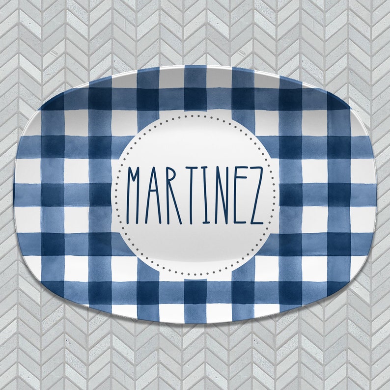 May include: A white oval serving platter with a blue and white gingham pattern. The platter has a circle in the center with the name "MARTINEZ" written in black.