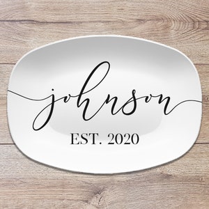 May include: White oval serving platter with the name "Johnson" in elegant black script. Below the name is "EST. 2020" in a simple black font. The platter is set against a light wood grain background.