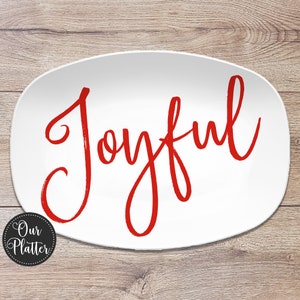 May include: White oval platter with the word "Joyful" in red script. The platter has a simple, elegant design, perfect for serving food. The platter is on a wooden surface.