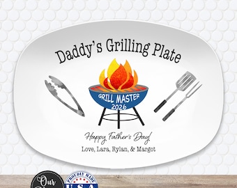 May include: A white oval serving platter featuring the text Daddy's Grilling Plate, a graphic of a blue grill with flames, the text Grill Master 2026, and the text Happy Father's Day! Love, Lara, Rylan, & Margot, flanked by grill tongs and a fork.