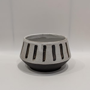 May include: A ceramic bowl with a white exterior and a dark brown base. Vertical dark brown stripes encircle the upper portion of the bowl. The bowl has a slightly flared shape.