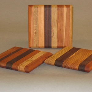 May include: Three wooden cutting boards with a striped pattern of light and dark wood. The boards are arranged in a row, with the largest board in the back and the two smaller boards in the front.