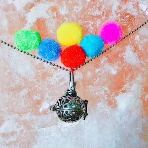 May include: A silver charm necklace with a decorative cage pendant. The necklace is adorned with five colorful pom-poms in shades of green, blue, yellow, red, and pink.