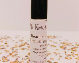 May include: A white roll-on bottle with a black cap. The label reads "Headache Aromatherapy" and lists the ingredients: "Grapeseed oil, Peppermint essential oil, *ORGANIC* 10 ml" and the website "www.keeleyorganics.com".