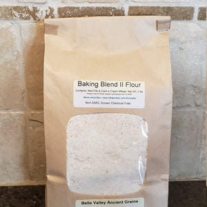May include: A brown paper bag with a clear window showing a beige flour inside. The bag is labeled "Baking Blend II Flour" with the contents listed as "Red Fife & Clark's Cream Wheat". The bag also states "Non GMO, Grown Chemical Free" and is from "Belle Valley Ancient Grains" in Newell, SD.