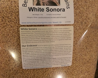 Könnte beinhalten: Nahaufnahme einer Tüte mit Weißem Sonora-Weizen, einer alten Getreidesorte. Die Tüte ist mit dem Namen des Weizens, dem Gewicht und der Website des Unternehmens beschriftet. Der Text auf der Tüte lautet "Belle Valley Ancient Grains, White Sonora, Nettogewicht: 3 lbs, Inhalt: Sonora-Weizen, www.bellevalleyancientgrains.com Newell, SD, Charge #1801".