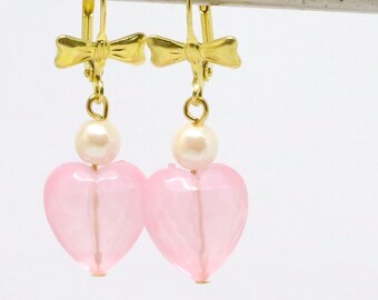 May include: A pair of pink heart-shaped earrings with a pearl accent and gold bow detail.