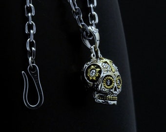 Op de afbeelding: Zilveren en gouden schedel hanger ketting met ingewikkelde details en een suiker schedel ontwerp. De ketting heeft een zilveren ketting met een karabijn sluiting.