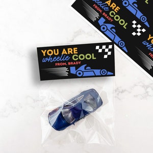 May include: A blue toy car in a clear plastic bag, with a black card that reads "YOU ARE wheelie COOL FROM, BRADY" in yellow, blue, and green. Additional cards with the same design are visible.