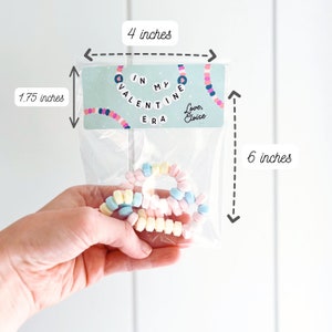May include: A clear plastic bag containing pastel-colored candy bracelets. The bag has a label that reads "IN MY VALENTINE ERA" with a decorative necklace design. The label is 4 inches wide and 1.75 inches tall. The bag is 6 inches tall.