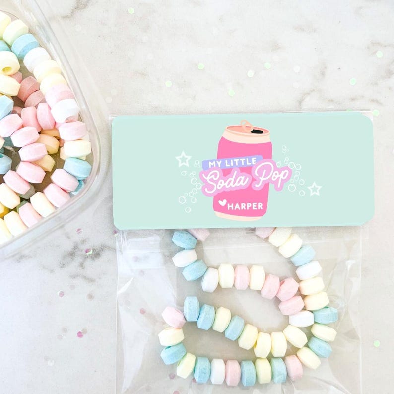 May include: A clear plastic container filled with pastel-colored candies. A candy necklace is in a clear plastic bag. The bag has a light blue label with the text "My Little Soda Pop" and a pink soda can illustration. The name "Harper" is below the text.