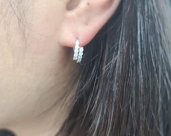May include: A pair of silver hoop earrings with a row of small clear cubic zirconia stones around the hoop.