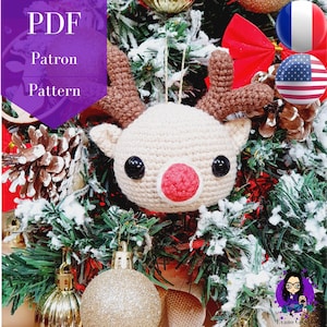 May include: Crochet reindeer ornament in beige with a red nose and black eyes. The ornament is hanging on a Christmas tree with gold ornaments and pine cones.