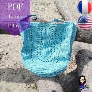 Op de afbeelding: Een lichtblauwe gehaakte tote bag met een uniek opengewerkt ontwerp. De tas ligt op een houten oppervlak met zand op de achtergrond. De tekst "PDF Patron Pattern" is zichtbaar in de linkerbovenhoek van de afbeelding.