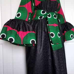 May include: A long black dress with a green and pink patterned top and a black belt. The sleeves are ruffled and the dress has a geometric pattern.