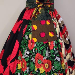May include: A vibrant, patchwork skirt featuring a variety of colorful African wax print fabrics. The skirt showcases bold patterns, including large red flowers on a black background, and a large bow at the waist.