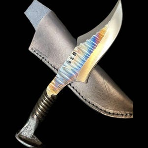 May include: A handmade knife with a rainbow-colored blade and a leather sheath. The handle is made from a repurposed railroad spike. The blade is marked with the letters "A.L.W."
