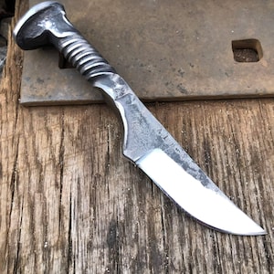 May include: A handmade knife with a twisted metal handle and a sharp, polished blade. The knife is made from a repurposed railroad spike.