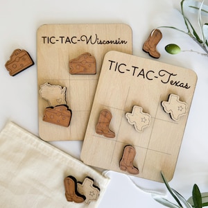 May include: Two wooden Tic-Tac-Toe boards with game pieces. One board says "Tic-Tac-Toe Wisconsin" and features cheese wedges and the state of Wisconsin. The other board says "Tic-Tac-Toe Texas" and features cowboy boots and the state of Texas.