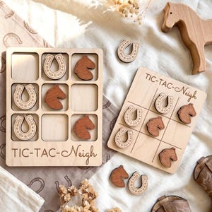 May include: Two light-colored wooden tic-tac-toe boards with the text TIC-TAC-Neigh engraved on the bottom. The game pieces consist of light-colored wooden horseshoes and darker brown wooden horse head shapes. A wooden horse figure is also present.