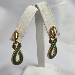 May include: Gold-tone earrings with a teal enamel infinity symbol design. The earrings are displayed on a white earring holder. The earrings have a teardrop-shaped top and a loop design.