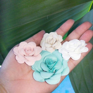 May include: Four paper flowers in different colors: pink, white, light blue, and a darker shade of blue. The flowers are arranged in a hand.