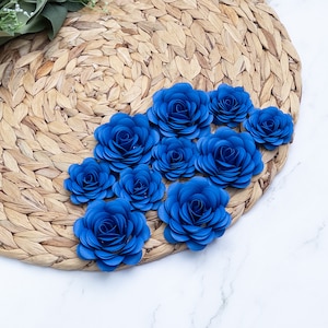 May include: A close-up of a set of blue paper flowers arranged on a woven straw placemat. The flowers are made of multiple layers of paper, creating a delicate and layered effect.