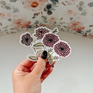 May include: A set of three floral stickers featuring pink and white flowers with black outlines. The stickers are on a white background.