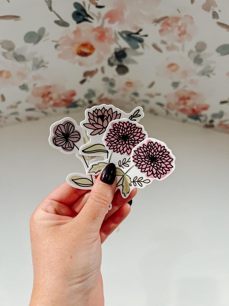 May include: A set of three floral stickers featuring pink and white flowers with black outlines. The stickers are on a white background.