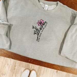 May include: A light gray sweatshirt with a black and pink floral design and the text "Bloom Where You Are Planted".