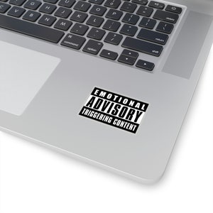 Può includere: Un adesivo bianco e nero con il testo "Emotional Advisory Triggering Content" su un laptop argentato.