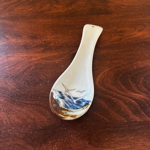 May include: White ceramic spoon rest with a blue and brown seascape design featuring seagulls in flight.
