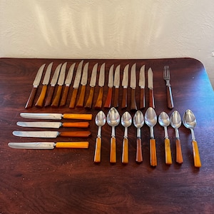 May include: A set of vintage silverware with brown and amber handles. The set includes 18 pieces: 12 knives, 6 spoons, and a fork. The silverware is arranged on a wooden surface.