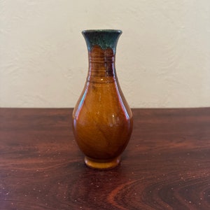 May include: A small, brown ceramic vase with a green glaze at the top. The vase has a rounded body and a narrow neck.
