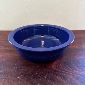 May include: A deep blue ceramic bowl with a rounded rim and a smooth, glossy finish. The bowl is empty and sits on a dark wood surface.
