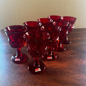 May include: Set of eight red glass wine goblets with a textured design. The goblets have a short stem and a round bowl.