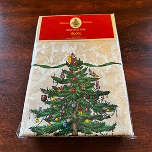 May include: A packaged Christmas Tree Spode tablecloth. The cream-colored cloth features a detailed illustration of a decorated Christmas tree with ornaments and Santa Claus. The top of the package is red with the words "Christmas Tree" and "Spode."