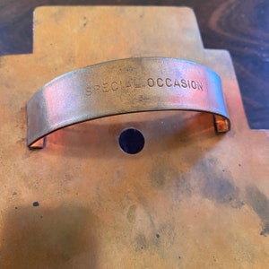 May include: A copper cookie cutter with a handle and the words "SPECIAL OCCASION" engraved on the handle.