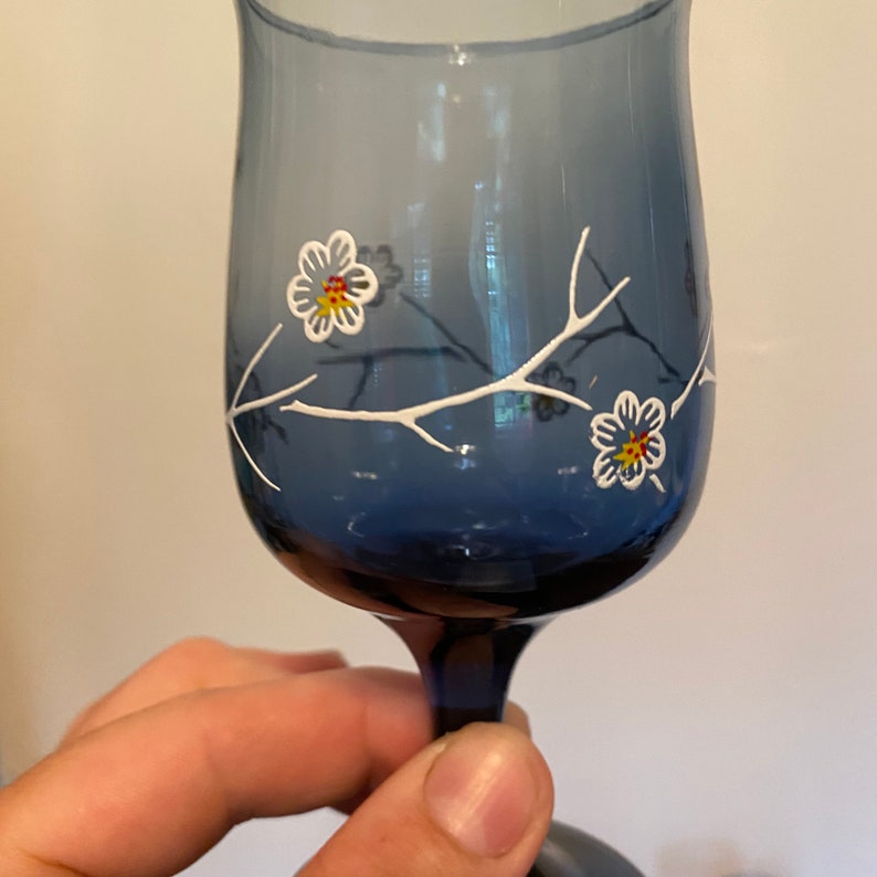 May include: A blue glass wine glass with a white floral design. The flowers have yellow and red centers.